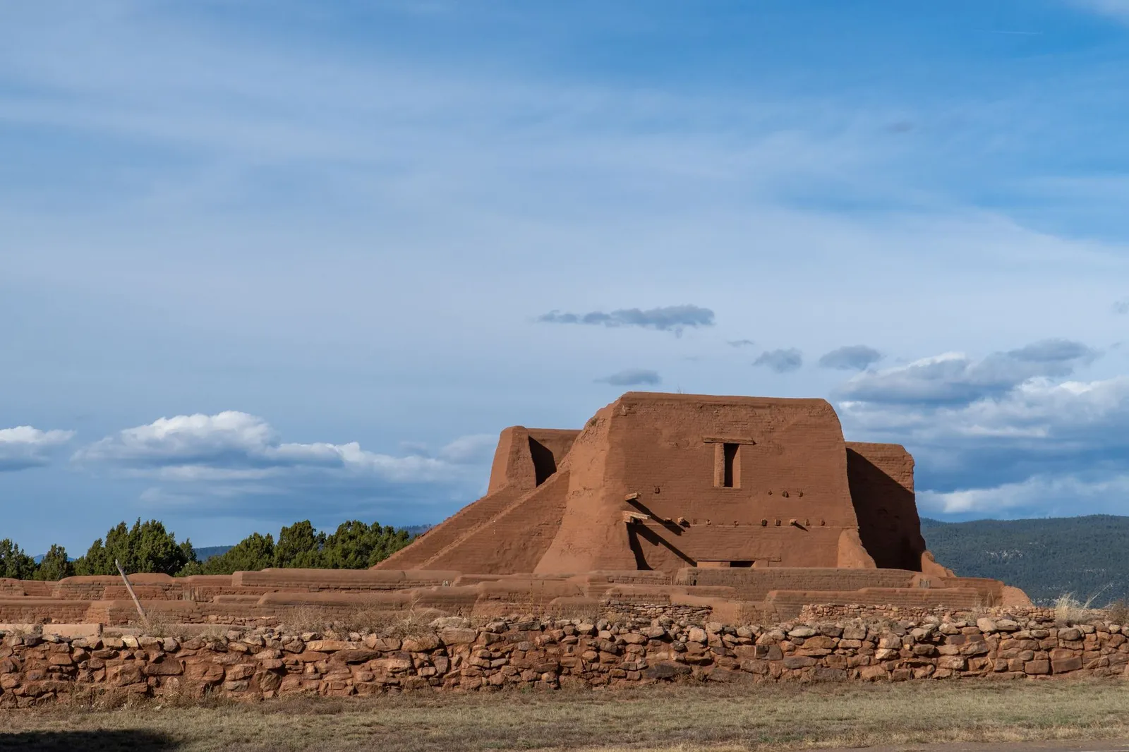 Adobe ruins at Pecos National Historical Park under a clear blue sky, with a low stone wall in the foreground