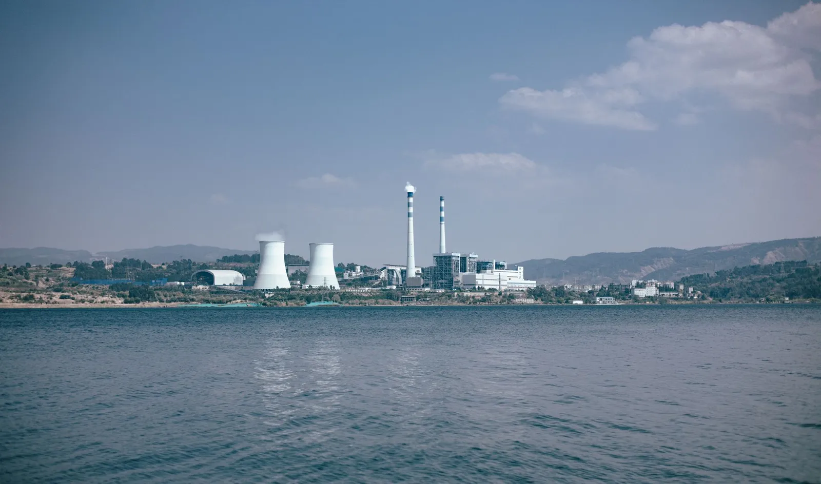 Power plant by a lake with cooling towers and smokestacks under a clear sky