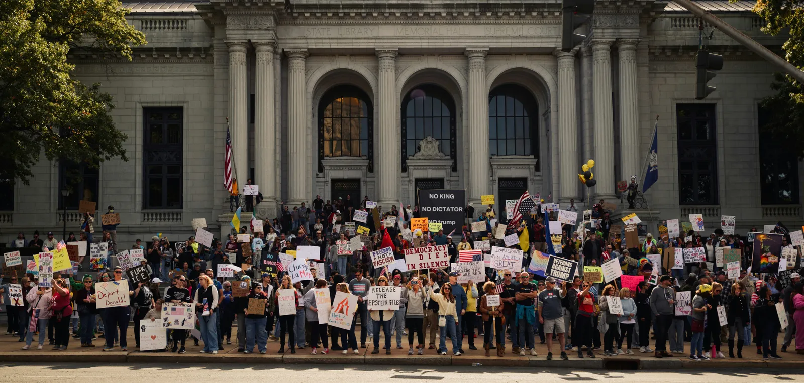 Crowd of protesters holding signs gathered on the steps of a civic building