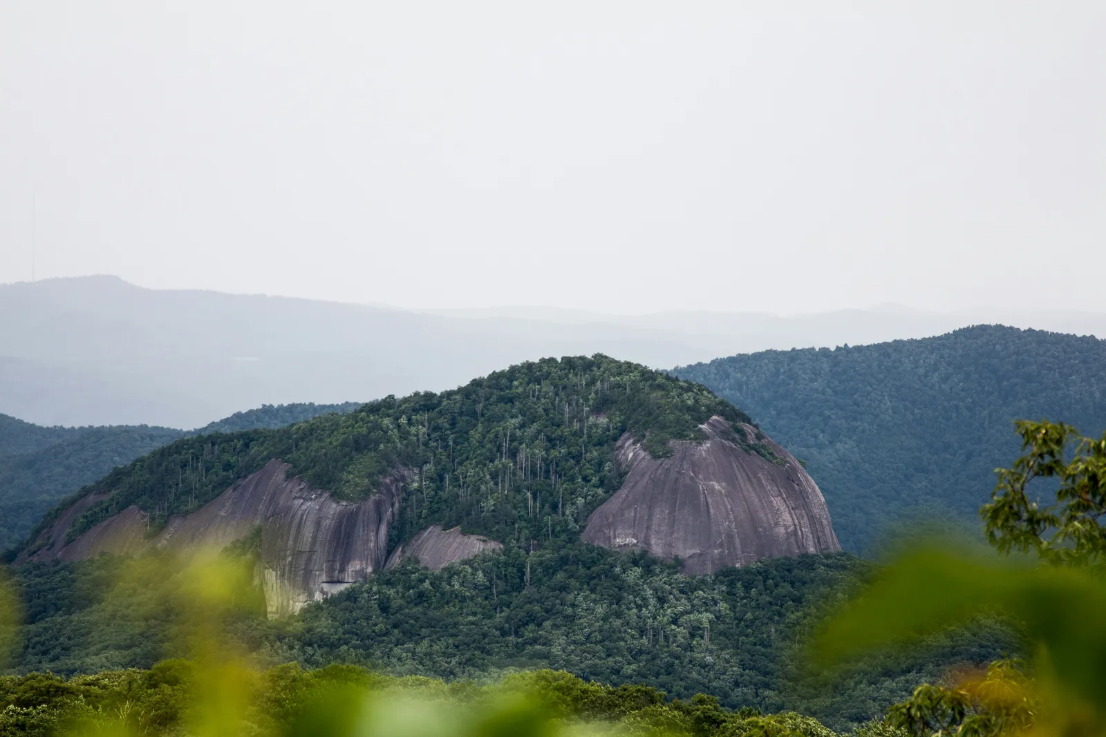 Looking Glass Rock rising above Pisgah National Forest, with forested Blue Ridge slopes under a hazy sky